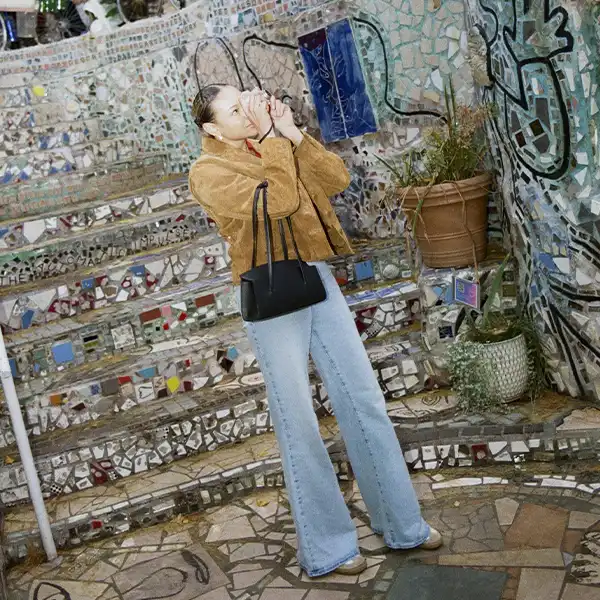 Woman in a brown jacket and light jeans taking photographs on a flint-strewn street