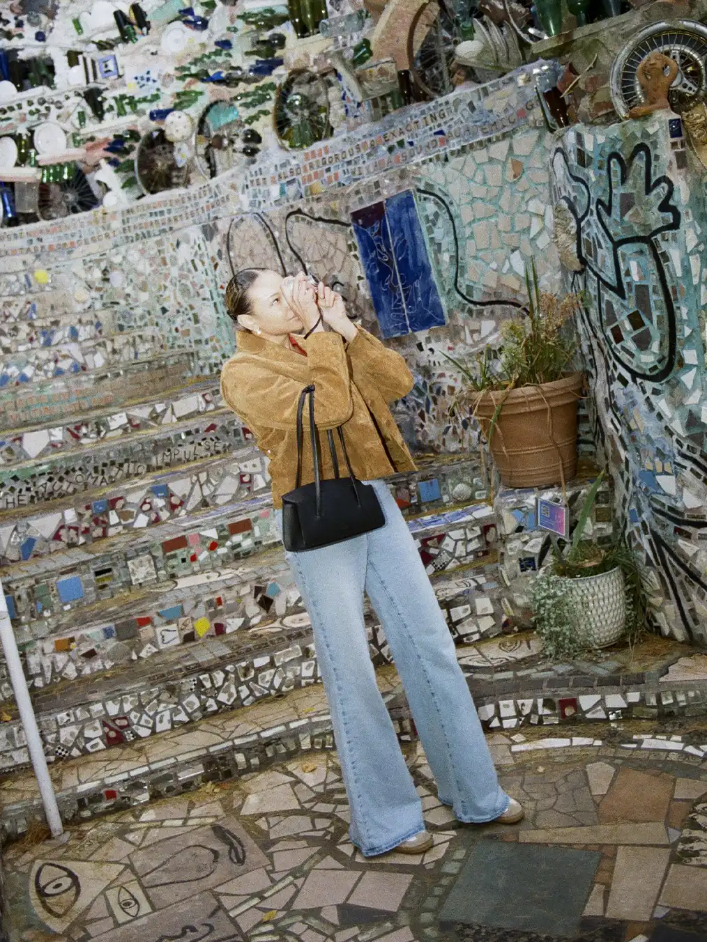 Woman in a brown jacket and light jeans taking photographs on a flint-strewn street