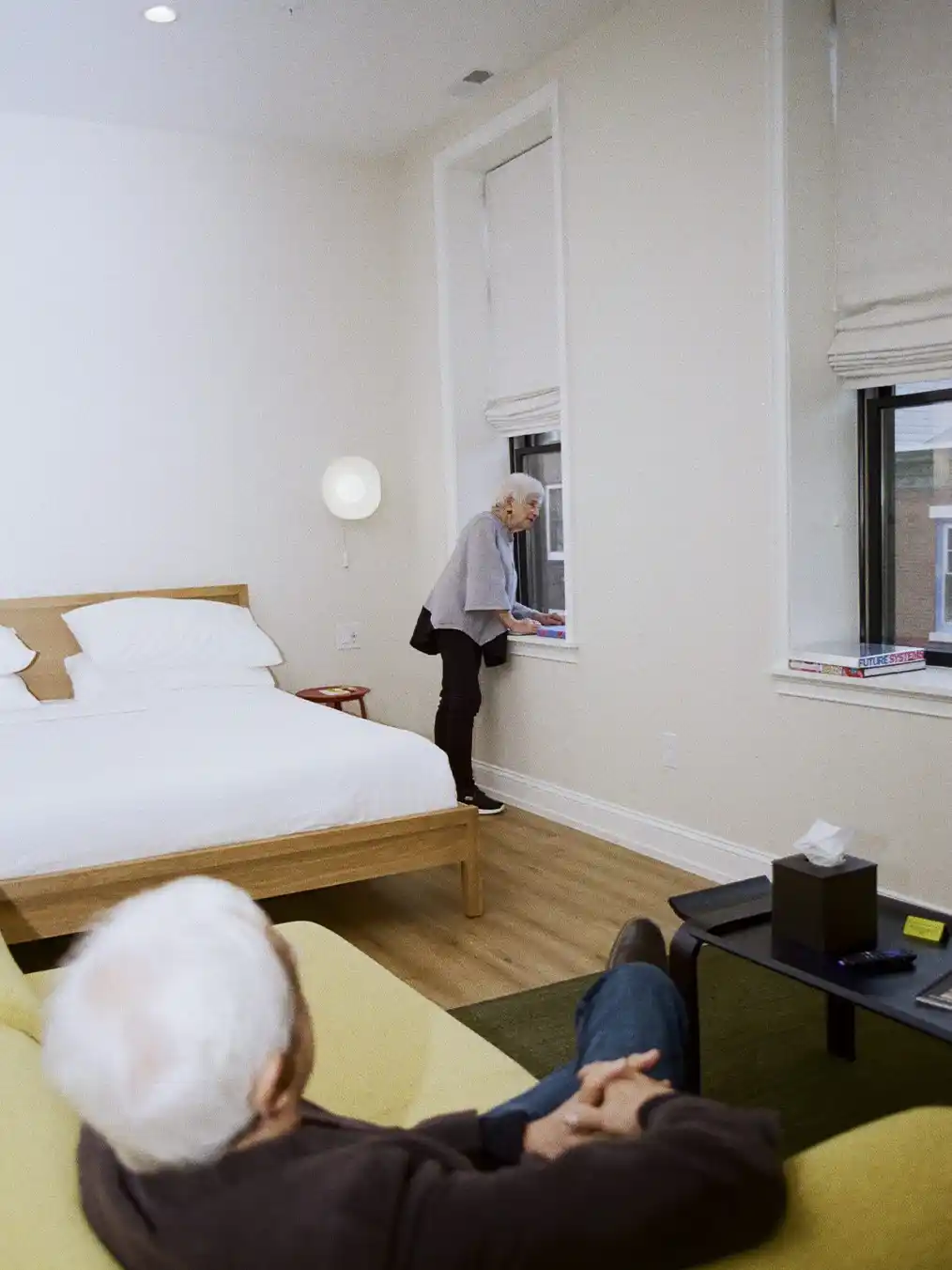 woman leaning out of window next to man sitting on yellow sofa