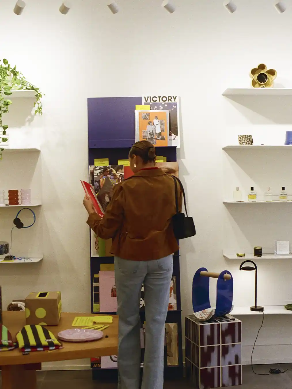 woman in a brown jacket and light jeans looking at objects in a store