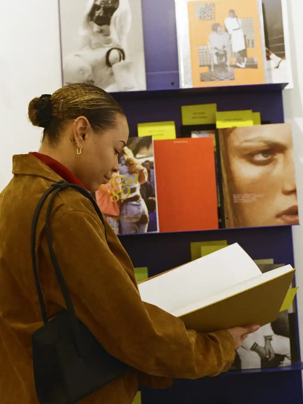 woman in a brown jacket and light jeans reading a book