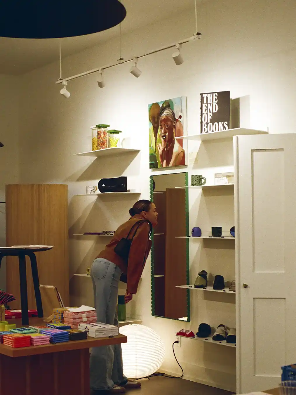 woman in a brown jacket and light jeans looking at objects in a store