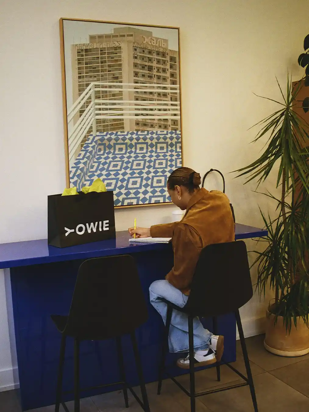 woman in a brown jacket and light jeans sitting in a cafe