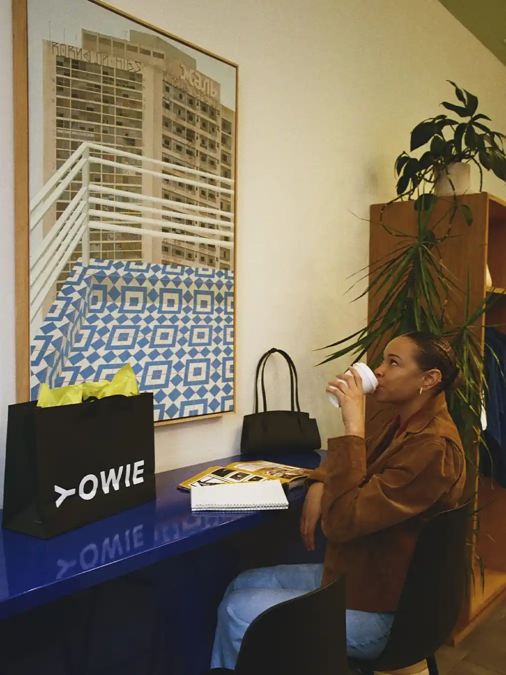woman in a brown jacket and light jeans drinking coffee