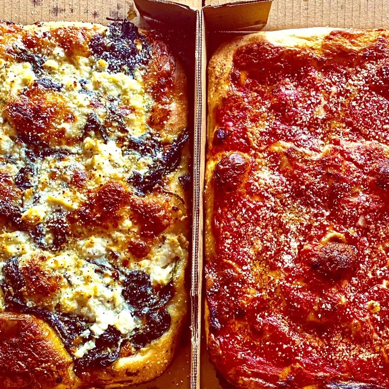 Two rectangular pizzas side by side in a box—one topped with melted cheese and pepperoni, and the other covered with a thick layer of bright red tomato sauce.